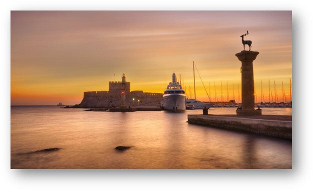 Sunset over Mandraki Harbor in Rhodes, Greece, with the fortress, boats, and deer statue
